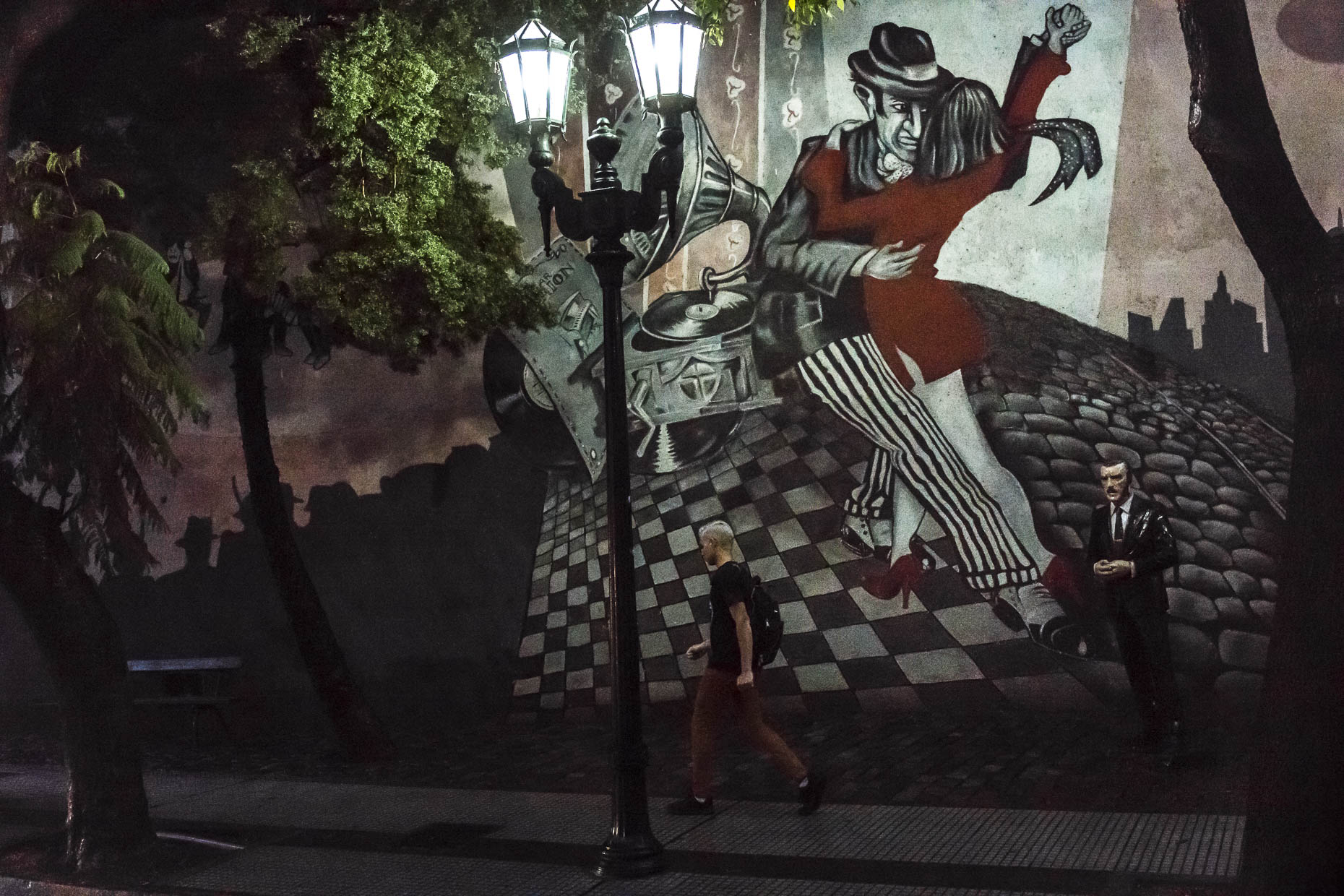 Man walks past a painted mural depicting a Tango dance scene.